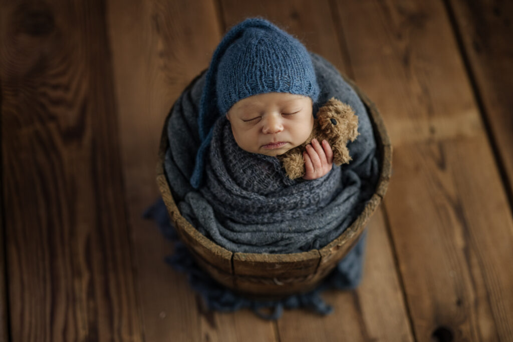 Infant photography featuring a boy in blue, cuddling a bear 