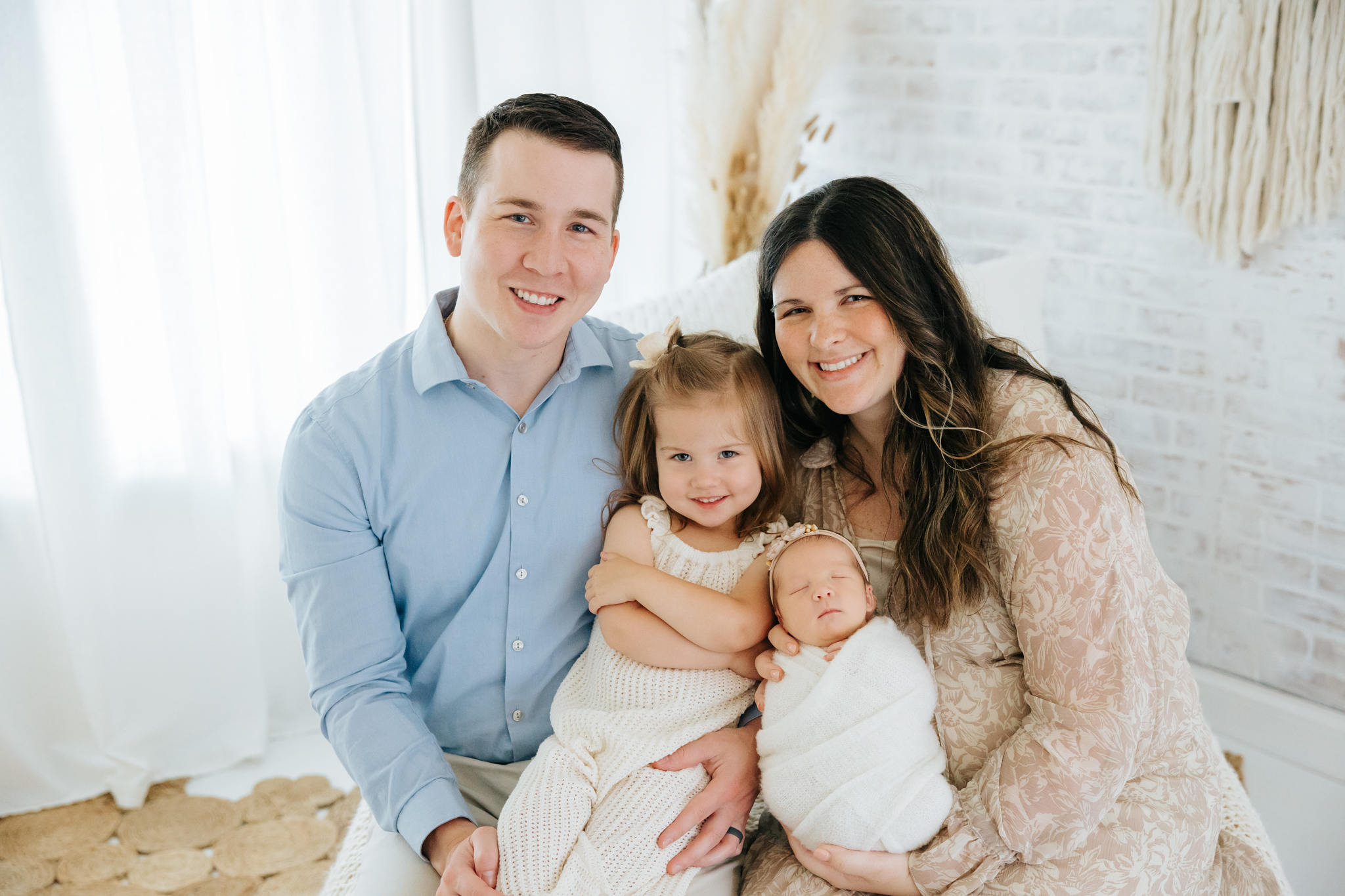 family pose with newborn on bed at Kelly Adrienne Photography