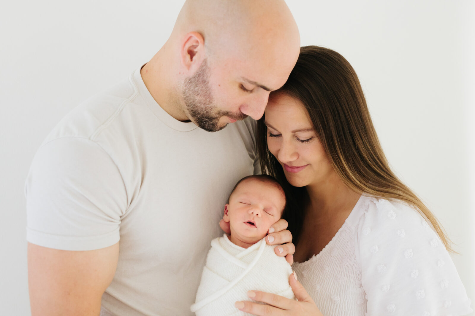 parents wearing white and looking down at their newborn