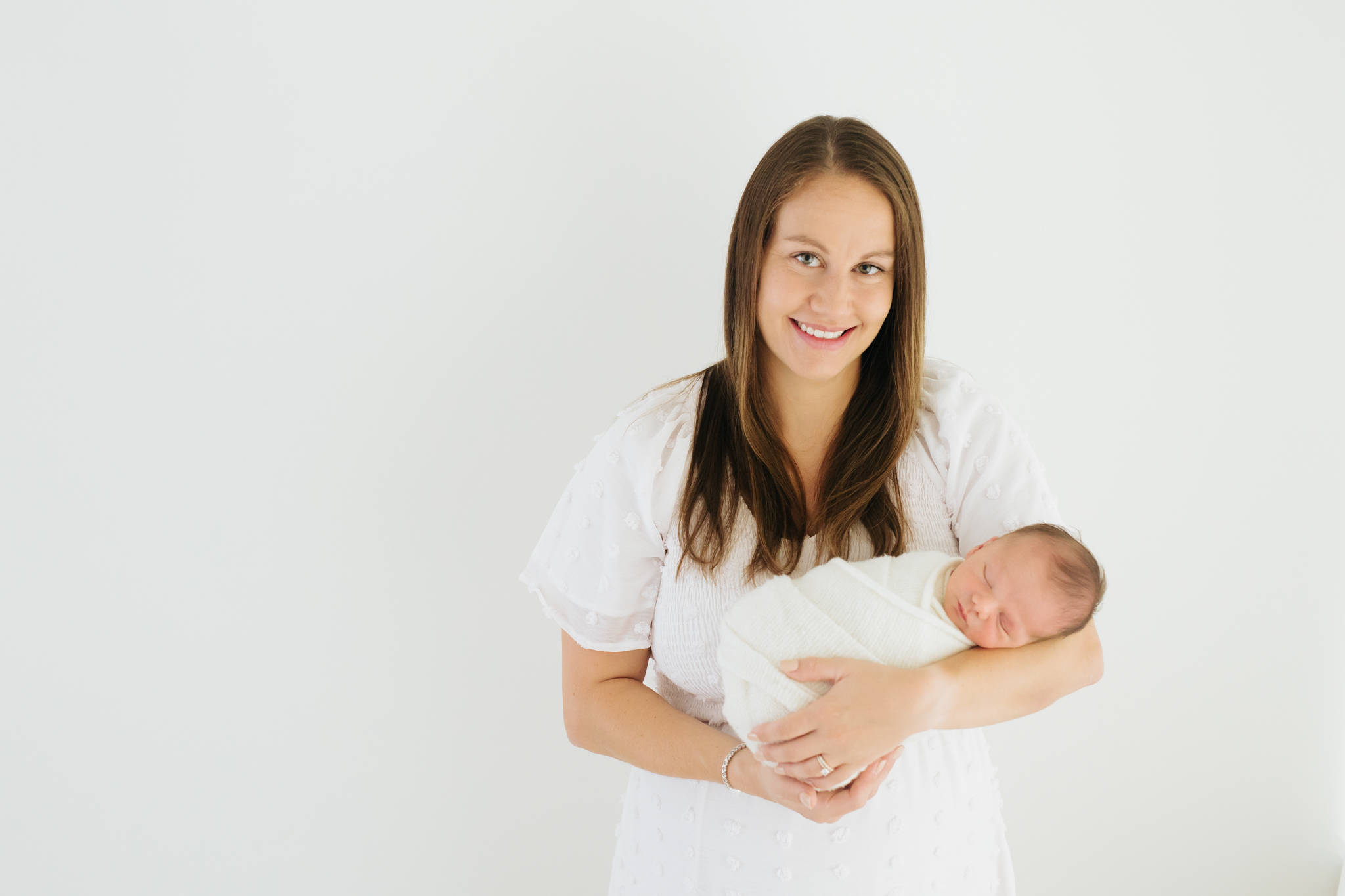 mother dressed in white holding her newborn baby and smiling at the camera