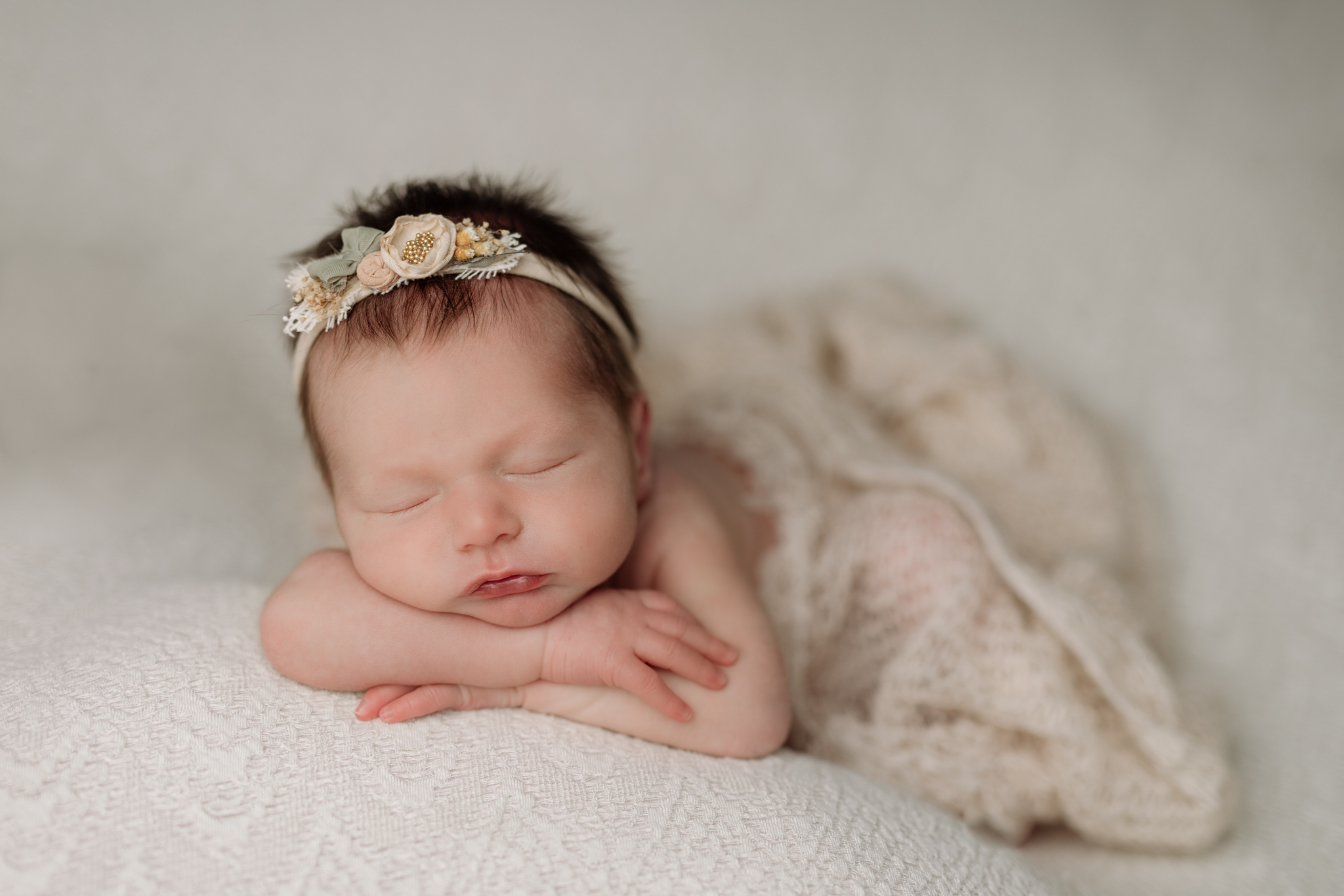 Newborn baby girl with head on hands on a cream lace backdrop