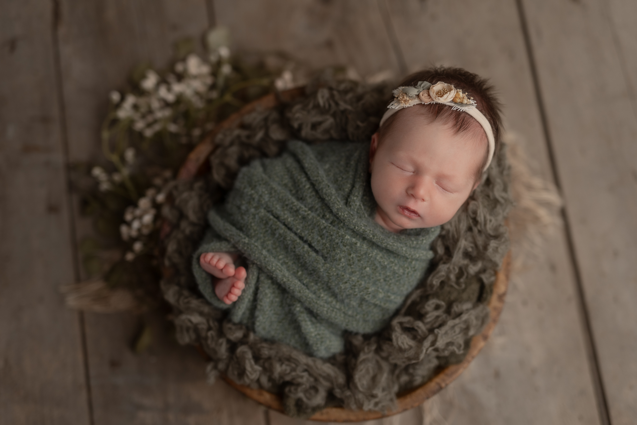 sleeping newborn baby girl wrapped in green with a matching headband, lying in a round bowl