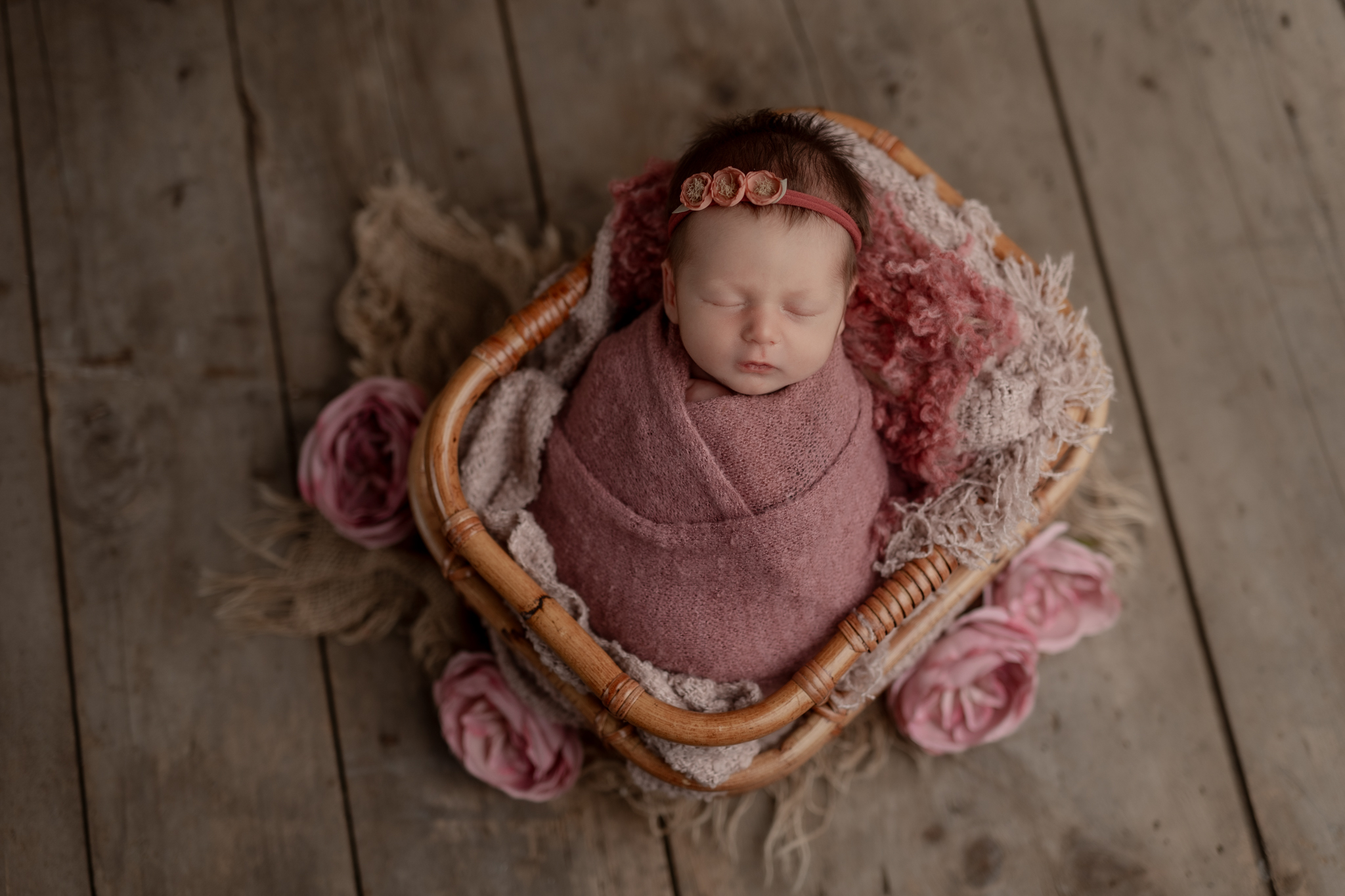 newborn baby girl sleeping in a basket prop wrapped in pink with a matching headband