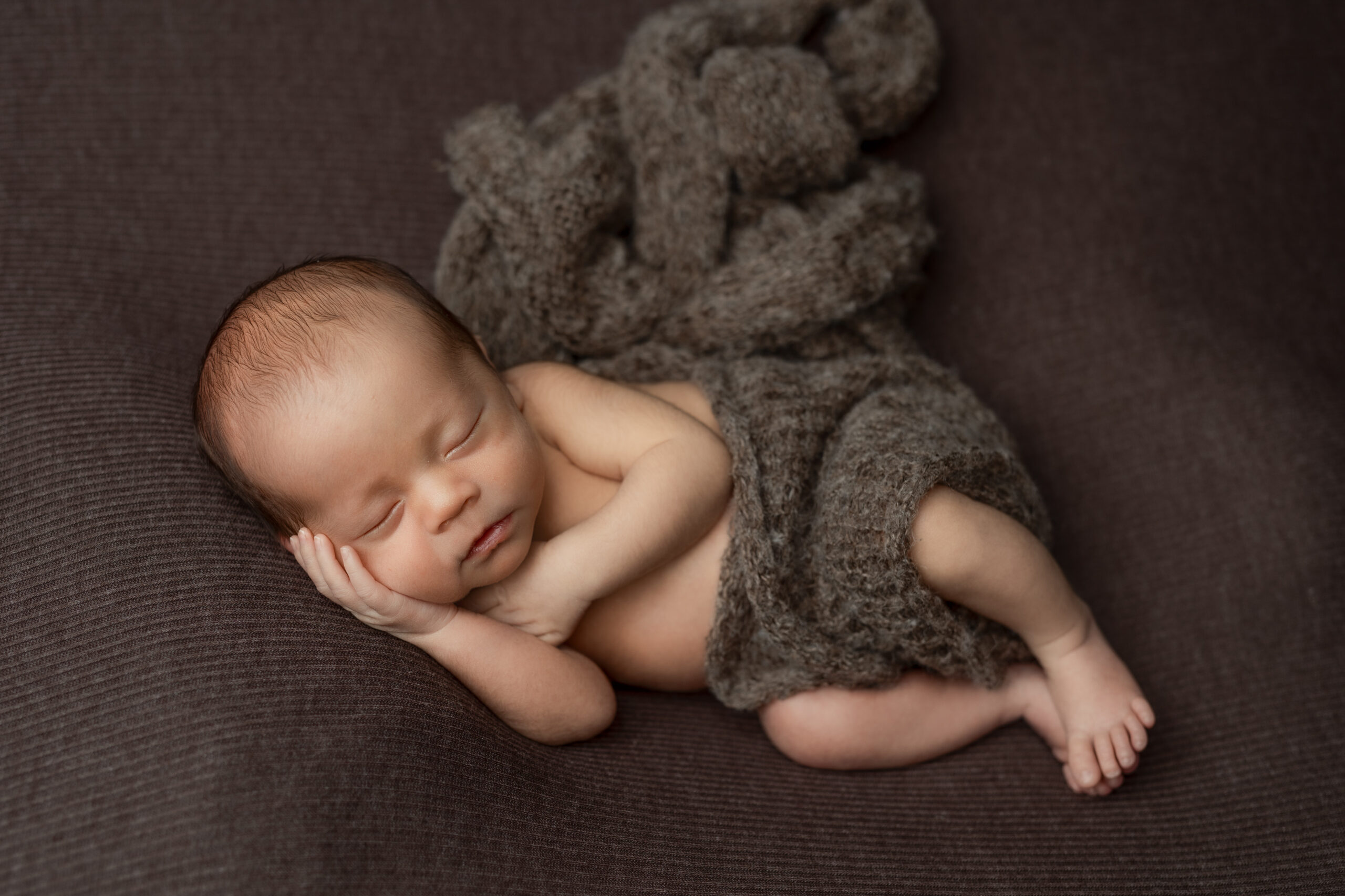 newborn boy in brown wrap on bron backdrop fabric