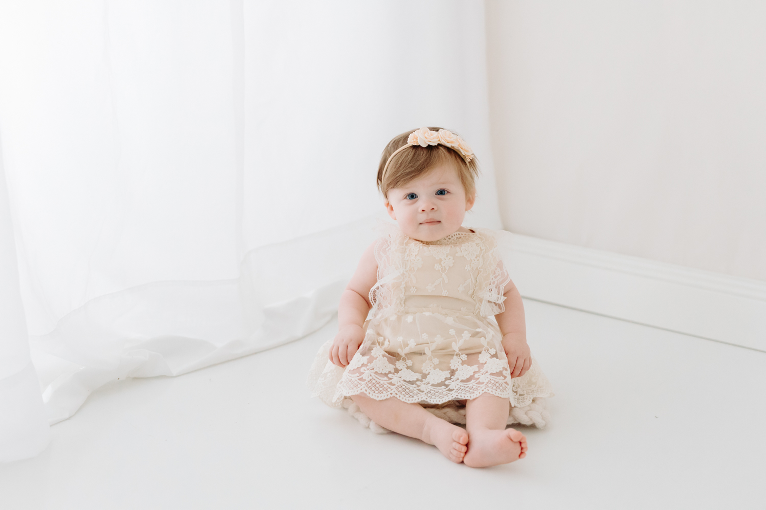 tips on working from home with a baby | one year old girl sits in front of a curtain dressed in white